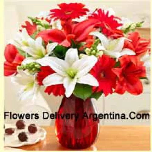 赤いガーベラ、白いユリ、赤いユリ、その他のアソートされた花々が美しくガラスの花瓶にアレンジされています